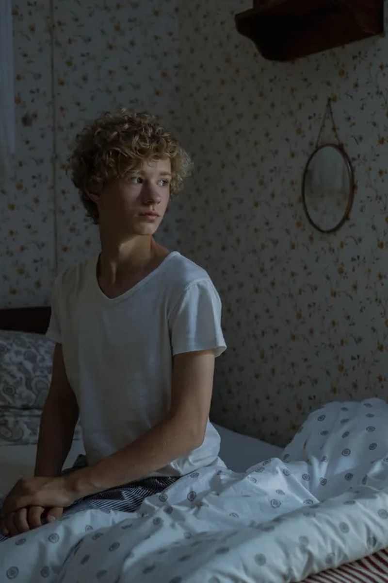 Teenage boy with curly blond hair in a casual bedroom portrait