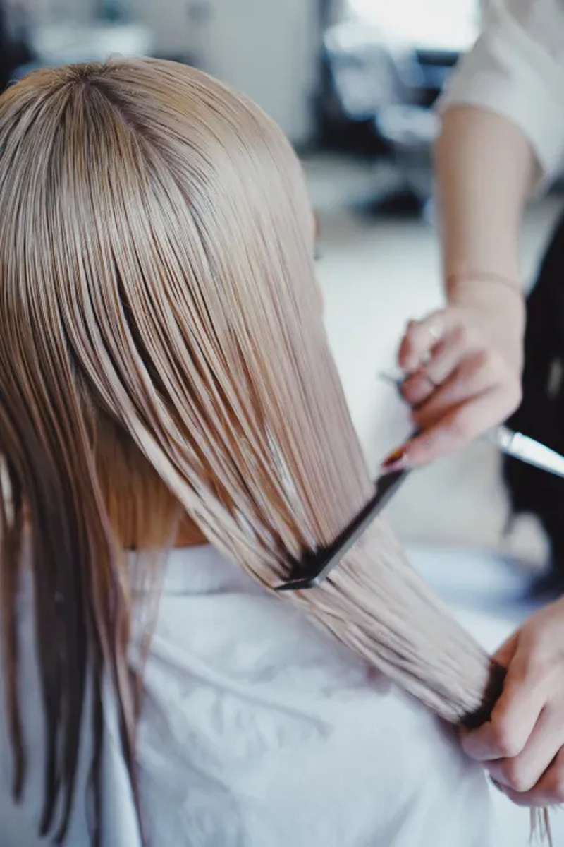 A close-up of long, clearly straight blonde hair being arranged in a salon.